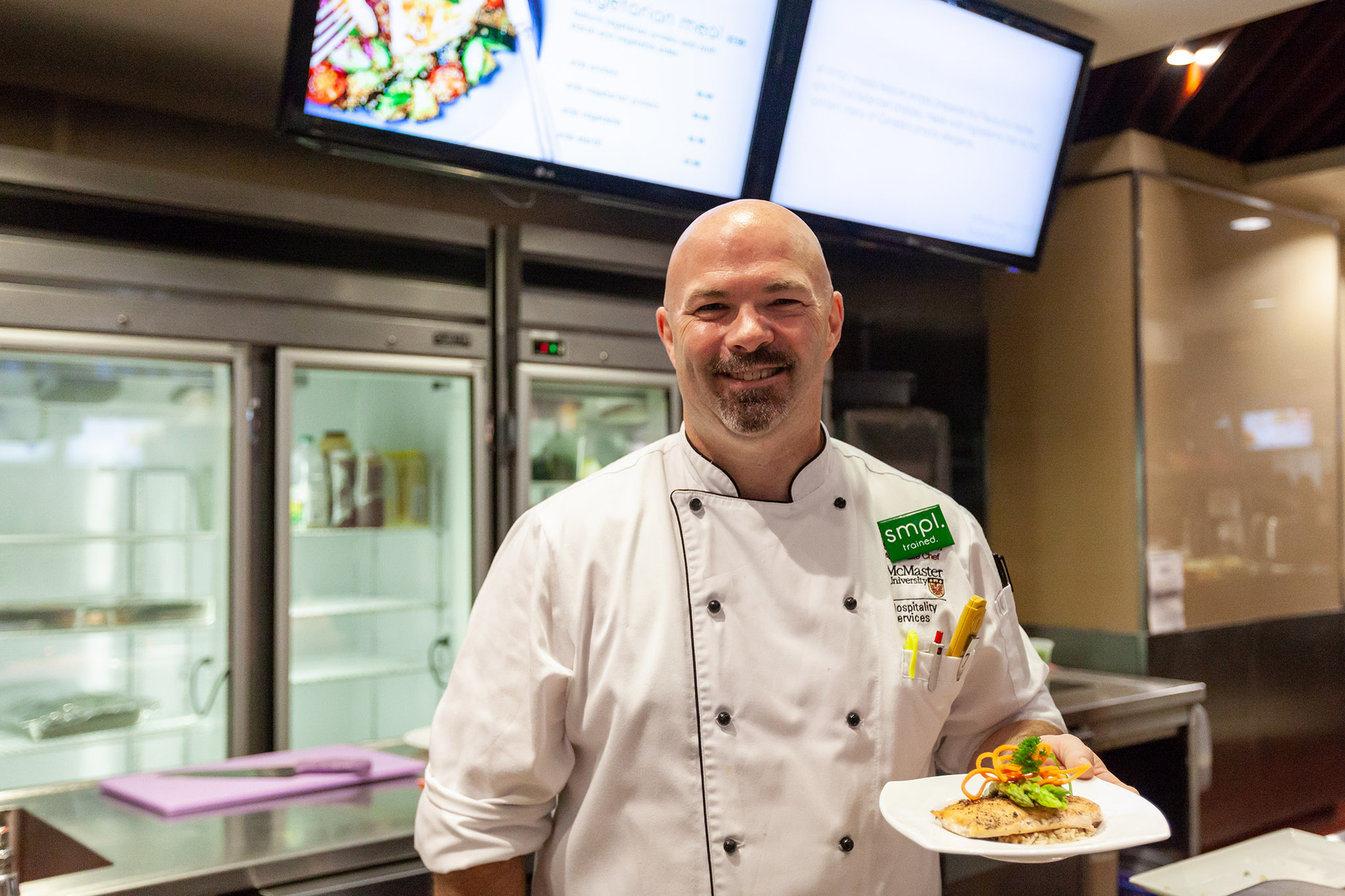 Photo of chef smiling holding plate of salmon and asparagus