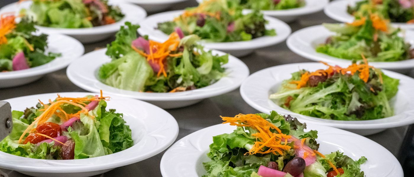 Several white bowls with mixed salad greens and shredded carrot